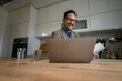 © Moon Safari - Low angle view of smiling young businessman in eyeglasses working over laptop on desk in home office