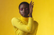 Close-up portrait of an African American woman with her hand near face in yellow clothing isolated on yellow background