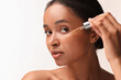 © New Africa - Beautiful woman applying serum onto her face on white background, closeup. Space for text