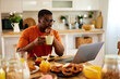 © Stockphotodirectors - Pensive black man working on laptop during breakfast at home