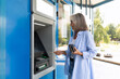 a mature gray-haired woman stands at an ATM and understands the electronic system