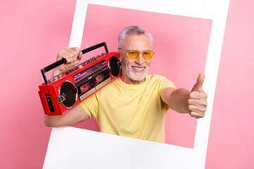 Poster - Portrait of funny pensioner person wear stylish t-shirt hold boombox on shoulder in frame show thumb up isolated on pink color background