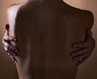 © LuneVA/peopleimages.com - Woman, back and hands touching body on brown background in studio for creative aesthetic, art deco and skin texture. Person, dark and shadow of model in self love hug for nude and sensual wellness