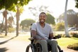 Smiling young African American man in a wheelchair enjoying the autumnal city park.