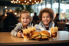 Two Happy Little American Children Boy And Girl Sit By The Table And Eat Delicious Hamburgers And Fries. Unhealthy Food Childhood Concepts And Eating.