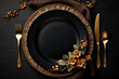 Golden cutlery on black background. Black empty ceramic plate with golden fork, spoon and knife. Fashionable and luxury eating. Flat-lay, top view. Copy space for your text.