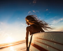 Out Of Focus Portrait Of Surfer Girl Holding Her Board In The Sea At Sunset