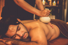 Hot Herbal Ball Spa Massage Body Treatment, Masseur Gently Compresses Herb Bag On Man Body. Tranquil And Serenity Of Aromatherapy Recreation In Warm Lighting Of Candles At Spa Salon. Quiescent