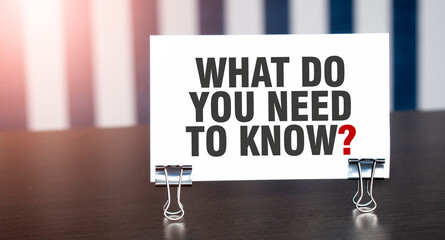 WHAT DO YOU NEED TO KNOW sign on paper on dark desk in sunlight. Blue and white background