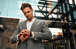 Modern attractive serious confident successful handsome adult bearded man looking at wristwatch waiting for business meeting with partner standing outside business center.Business concept.
