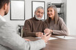 © New Africa - Elderly couple consulting insurance agent about pension plan at wooden table indoors