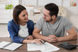 © New Africa - Young couple with papers discussing pension plan at wooden table indoors