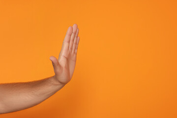 Man showing stop gesture on orange background, closeup with space for text