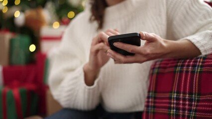 Sticker - Young caucasian woman using smartphone sitting by christmas tree at home