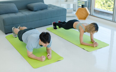 Wall Mural - Asian young fit male female husband and wife in sportswear sport bra legging stretching body lay down planking on elbows exercising practicing working out abdomen abs on yoga pilates in living room.