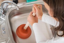 Woman Using Plunger In Sink