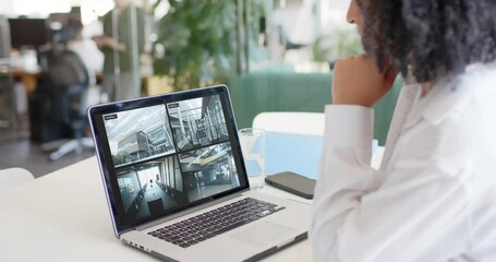 Poster - Biracial female security officer watching cctv camera views on laptop in office, slow motion