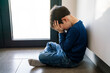 © cunaplus - Upset problem child with head in hands sitting on floor concept for bullying, depression stress or frustration at school