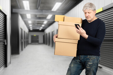 Wall Mural - Man near storage room. Businessman with boxes. Guy rents storage room. Man with telephone in warehouse building. Male standing near closed storage room. Corridor with gates in warehouse units