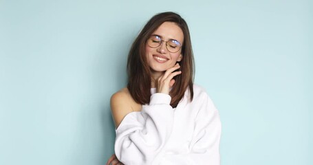 Wall Mural - Portrait of flirty young caucasian woman looking at camera with seductive facial expression. Slim beautiful lady in eyeglasses posing on blue background smiling. Sensual woman touch her face.