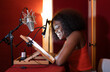 © ADDICTIVE STOCK - Smiling young black woman sitting at desk and recording podcast