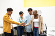 © ADDICTIVE STOCK - Cheerful multiracial colleagues standing together and stacking hands in office