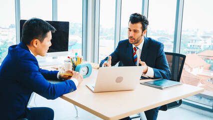 Two business people talk project strategy at office meeting room. Businessman discuss project planning with colleague at modern workplace while having conversation and advice on financial report. Jivy