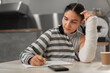© Andrii Lysenko - Beautiful girl with broken arm is making notes in cafeteria. Freelance and remote work. Modern female lifestyle