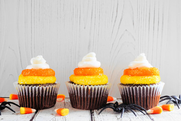 Poster - Halloween candy corn chocolate cupcakes in a row against a white wood background
