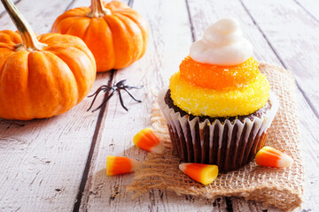 Poster - Halloween candy corn chocolate cupcake. Close up against a white wood background.