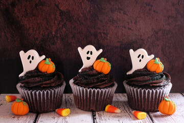 Poster - Spooky Halloween chocolate cupcakes with ghosts and pumpkins in a row against a dark wood background