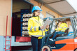 © Kzenon - woman in industrial gear standing in front of a forklift transporting goods from a warehouse