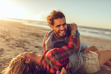 Young couple on a date having fun on a sandy beach next to the ocean during sunset