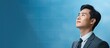 © vxnaghiyev - Asian man in formal suit working in office gaze directed towards copy space on blue background