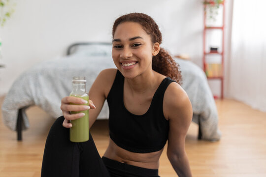 Portrait of young latin woman drinking detox smoothie made with fruits and vegetables after fitness workout routine at home. Fitness and healthy lifestyle concept
