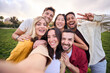 © CarlosBarquero - Group of young cheerful multi-ethnic friends taking selfie with mobile phone outdoor. Happy people together smiling and enjoying free time in park. Positive and fun youth relationships in community.