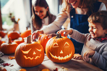 Happy Family Carving Pumpkins For Halloween. Mother, Father And Their Children Having Fun At Home. Selective Focus.  