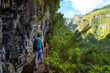 © Michael - Backpacker walks along a picturesque hike trail under a large steep rock face along a water channel through Madeira rainforest. Levada of Caldeirão Verde, Madeira Island, Portugal, Europe.