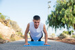 Young Caucasian man does push-ups on his mat in a public park. The effort is visible on his face.