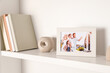 © New Africa - Photo frame with family portrait and books on white shelf indoors