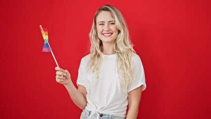 Poster - Young blonde woman smiling confident holding rainbow flag over isolated red background