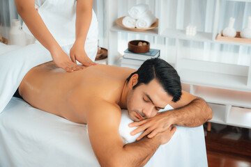 Caucasian man customer enjoying relaxing anti-stress spa massage and pampering with beauty skin recreation leisure in day light ambient salon spa at luxury resort or hotel. Quiescent