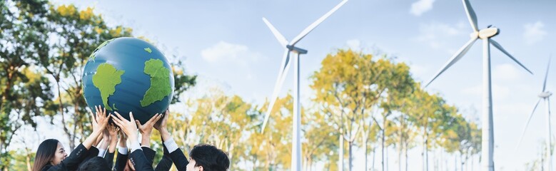 Earth day concept with big Earth globe held by asian business people team promoting environmental awareness using clean sustainable and renewable energy with wind turbine for greener future. Gyre