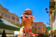 Woman s hand holding artisanal chocolate gelato in a cone, view of traditional colorful houses in the Old Town Vieille Ville of Menton South of France
