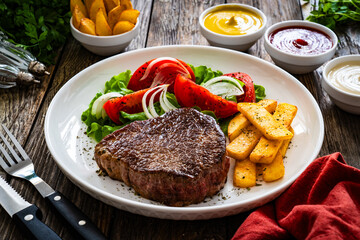 Wall Mural - Grilled beef steak with French fries and fresh vegetables on wooden table
