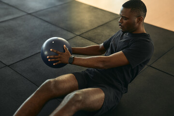 Wall Mural - Strong black sportsman doing abs exercise with medicine ball in gym