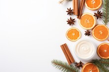 A Flat Lay View Of A Christmas-themed Beauty Arrangement On A White Background, Consisting Of Cosmetic Cream Containers, Dried Orange Slices, Cinnamon Sticks, And Fir Branches.