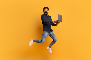 Happy indian man with laptop computer jumping up over yellow background