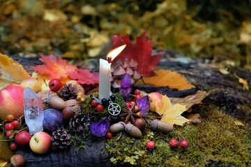 Sticker - autumn background. Candle with amulet, crystals, fall leaves, fruits, berries, nuts in forest, natural background. Wiccan altar for Mabon sabbat. autumn equinox. Witchcraft, esoteric spiritual ritual