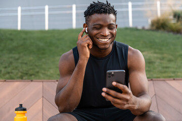 Canvas Print - Happy African man in sportswear listening to the music while resting after sport training outdoors